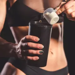 Kobieta dodaje proszek proteinowy do shakera.