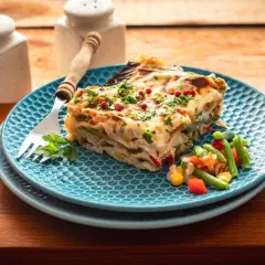 Kawałek pysznej, warzywnej lasagne na niebieskim talerzu, posypany natką i pieprzem. To bardzo dobry przepis na lazanię, który zachwyci każdego!