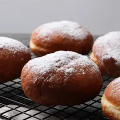 Szybkie pączki z piekarnika, oprószone cukrem pudrem, wyglądają apetycznie na czarnej kratce.