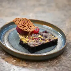 Elegancka monoporcja: czekoladowy brownie z malinami, sorbetem malinowym i dekoracją z listka.