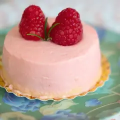 Delikatny krem malinowy z mascarpone do tortu, ozdobiony dwoma świeżymi malinami i gałązką rozmarynu, na zielonym talerzyku w kwiaty.