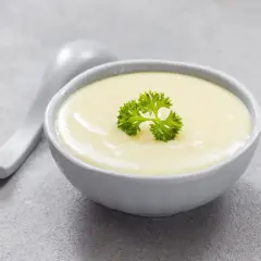 Kremowa zupa, idealna na dietę bezresztkową, ozdobiona natką pietruszki. Obok leży biała łyżka.