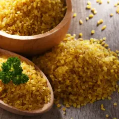 Kasza bulgur na drewnianym stole, z gałązką pietruszki. Niska wartość indeksu glikemicznego sprawia, że jest zdrowym wyborem.