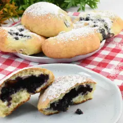 Pyszne, domowe jagodzianki posypane cukrem pudrem, jedna przekrojona, ukazująca soczyste nadzienie.