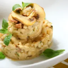 Kremowe risotto z grzybami, podane w formie wieży, ozdobione świeżymi ziołami i plasterkami pieczarek. Idealne danie z ryżu do risotto.