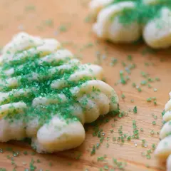 Kruche ciasteczka w kształcie choinek, posypane zielonym cukrem, na drewnianym tle.