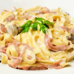 Tagliatelle z szynką i pieczarkami w kremowym sosie, z dodatkiem mozzarelli. Udekorowane natką pietruszki.