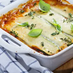 Pyszne, zapiekane w białym naczyniu danie, gdzie cienkie plastry cukinii zastępują makaron w lasagne. Całość polana sosem pomidorowym i posypana serem, udekorowana listkami bazylii i tymianku.