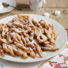 Chrupiące faworki, przepis babci, posypane cukrem pudrem, na talerzu.
