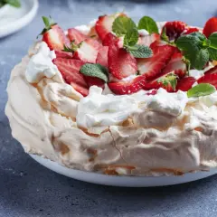Puszysty tort bezowy z mascarpone i bitą śmietaną, ozdobiony świeżymi truskawkami i miętą.