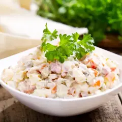 Sałatka jarzynowa w białej misce, udekorowana natką pietruszki. Zastanawiasz się, ile kcal ma sałatka jarzynowa?