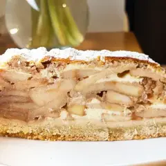 Pyszny kawałek szarlotki z warstwami jabłek i kremu, posypany cukrem pudrem. Idealna na deser, aż chce się ją piec!