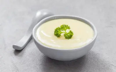 Kremowa zupa, idealna na dietę bezresztkową, ozdobiona natką pietruszki. Obok leży biała łyżka.