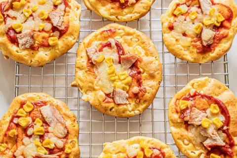 Mini pizze z serka wiejskiego, z kukurydzą i kawałkami mięsa, ułożone na metalowej kratce.