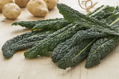 Kępy ciemnozielonego jarmużu i ziemniaki na drewnianym blacie.