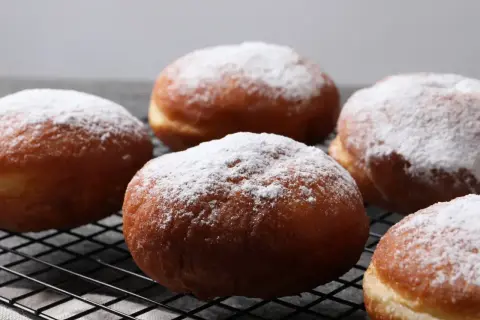 Szybkie pączki z piekarnika, oprószone cukrem pudrem, wyglądają apetycznie na czarnej kratce.