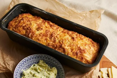 Chrupiąca babka ziemniaczana w keksówce, obok miseczka z masłem ziołowym.