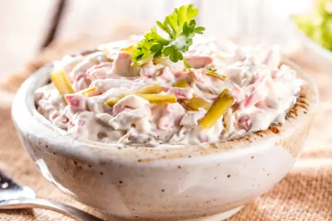Niemiecka sałatka ziemniaczana z ogórkiem i jajkiem, kremowa i pyszna, ozdobiona natką pietruszki.