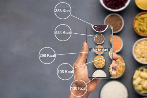 Dłoń trzyma smartfon z aplikacją do liczenia kalorii. Na ekranie widać różne produkty spożywcze i ich kaloryczność, pomocne przy diecie 1500 kcal.