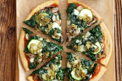 Pyszna pizza ze szpinakiem, cukinią i grzybami, polana zielonym pesto.