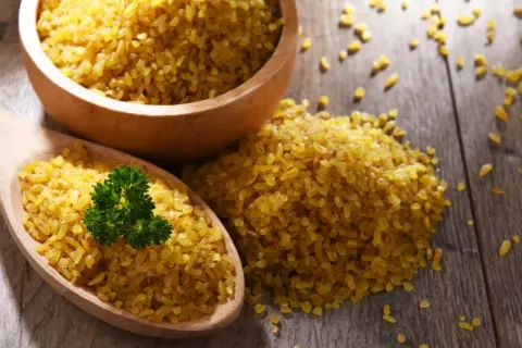 Kasza bulgur na drewnianym stole, z gałązką pietruszki. Niska wartość indeksu glikemicznego sprawia, że jest zdrowym wyborem.