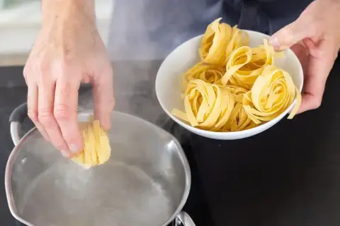 Ręce wkładają świeży makaron do wrzącej wody. Gotowanie makaronu to pierwszy krok do pysznego posiłku.