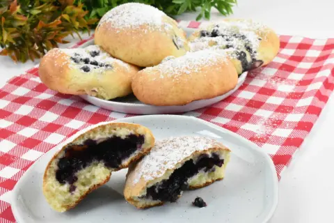 Pyszne, domowe jagodzianki posypane cukrem pudrem, jedna przekrojona, ukazująca soczyste nadzienie.