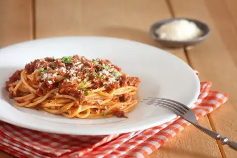 Porcja spaghetti bolognese, posypana parmezanem i natką pietruszki. Idealne na obiad, z uwzględnieniem spaghetti bolognese kcal.