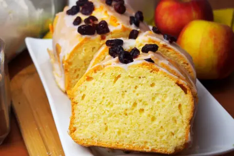 Pyszna, wilgotna babka cytrynowa z lukrem i żurawiną, obok jabłka.
