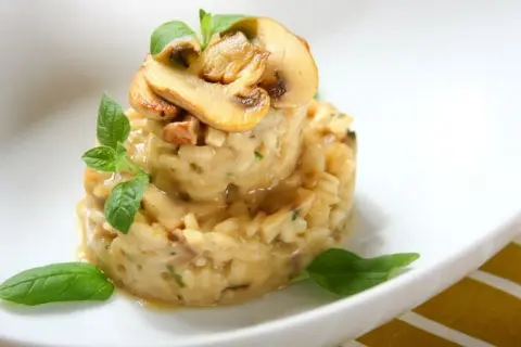 Kremowe risotto z grzybami, podane w formie wieży, ozdobione świeżymi ziołami i plasterkami pieczarek. Idealne danie z ryżu do risotto.