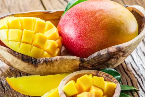 Soczyste mango, pokrojone w kostkę i w całości, w drewnianych miseczkach. Idealne na zdrową przekąskę, z niskim mango kcal.