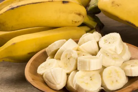 Kawałki banana na drewnianej misce, obok całe owoce. Idealna przekąska, gdy zastanawiasz się nad banan kcal.