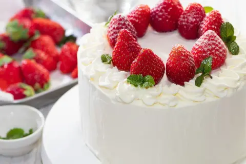 Puszysty tynk do tortu z mascarpone, ozdobiony świeżymi truskawkami i listkami mięty. Idealny na letnie przyjęcie.