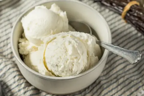 Puszyste lody z mascarpone w miseczce, gotowe do schrupania. Obok leżą laski wanilii.