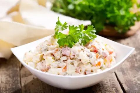 Sałatka jarzynowa w białej misce, udekorowana natką pietruszki. Zastanawiasz się, ile kcal ma sałatka jarzynowa?