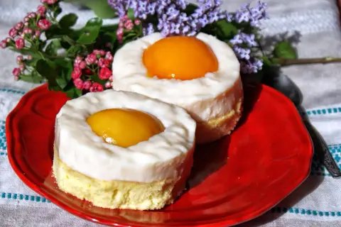 Dwa okrągłe ciastka z biszkoptem, kremem i brzoskwinią na czerwonym talerzu. Wyglądają jak ciasto jajko sadzone.