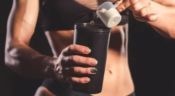 Kobieta dodaje proszek proteinowy do shakera.