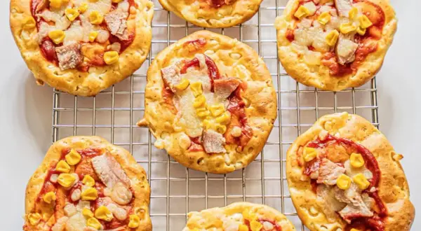 Mini pizze z serka wiejskiego, z kukurydzą i kawałkami mięsa, ułożone na metalowej kratce.