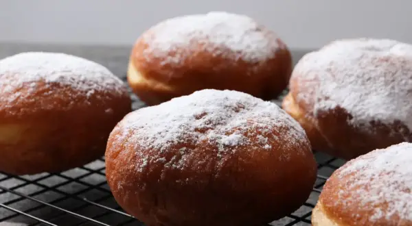 Szybkie pączki z piekarnika, oprószone cukrem pudrem, wyglądają apetycznie na czarnej kratce.