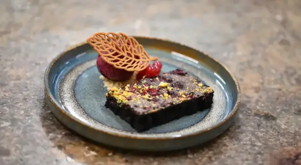 Elegancka monoporcja: czekoladowy brownie z malinami, sorbetem malinowym i dekoracją z listka.