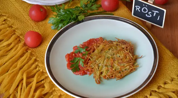 Chrupiące rosti ziemniaczane z pomidorami i natką pietruszki na talerzu, obok tabliczka z napisem "Rösti".