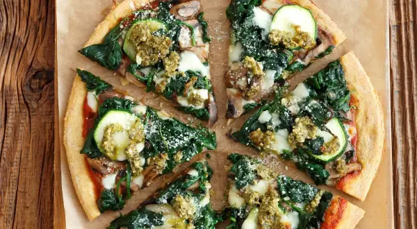 Pyszna pizza ze szpinakiem, cukinią i grzybami, polana zielonym pesto.