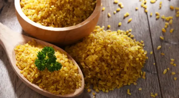 Kasza bulgur na drewnianym stole, z gałązką pietruszki. Niska wartość indeksu glikemicznego sprawia, że jest zdrowym wyborem.