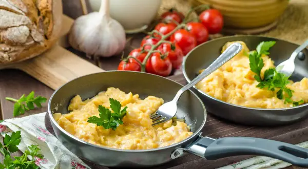 Pyszna jajecznica z 2 jajek, podana na patelni z natką pietruszki. Zastanawiasz się, ile kcal ma jajecznica z 2 jajek? To idealny początek dnia!