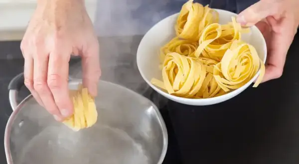 Ręce wkładają świeży makaron do wrzącej wody. Gotowanie makaronu to pierwszy krok do pysznego posiłku.