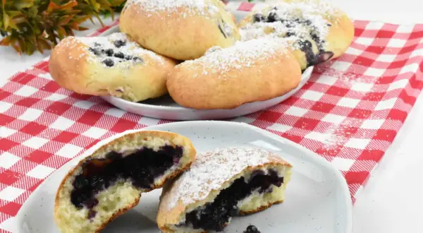 Pyszne, domowe jagodzianki posypane cukrem pudrem, jedna przekrojona, ukazująca soczyste nadzienie.