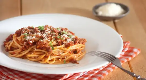 Porcja spaghetti bolognese, posypana parmezanem i natką pietruszki. Idealne na obiad, z uwzględnieniem spaghetti bolognese kcal.