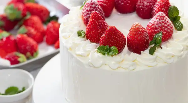 Puszysty tynk do tortu z mascarpone, ozdobiony świeżymi truskawkami i listkami mięty. Idealny na letnie przyjęcie.