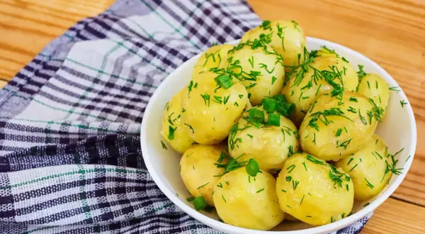 Młode ziemniaki w misce, posypane koperkiem i szczypiorkiem. Idealne na lato, a ile gotować młode ziemniaki? Krótko!