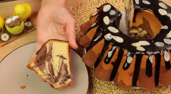 Najbardziej wilgotna babka w paski, polana czekoladą i posypana płatkami migdałów, z kawałkiem na talerzu.